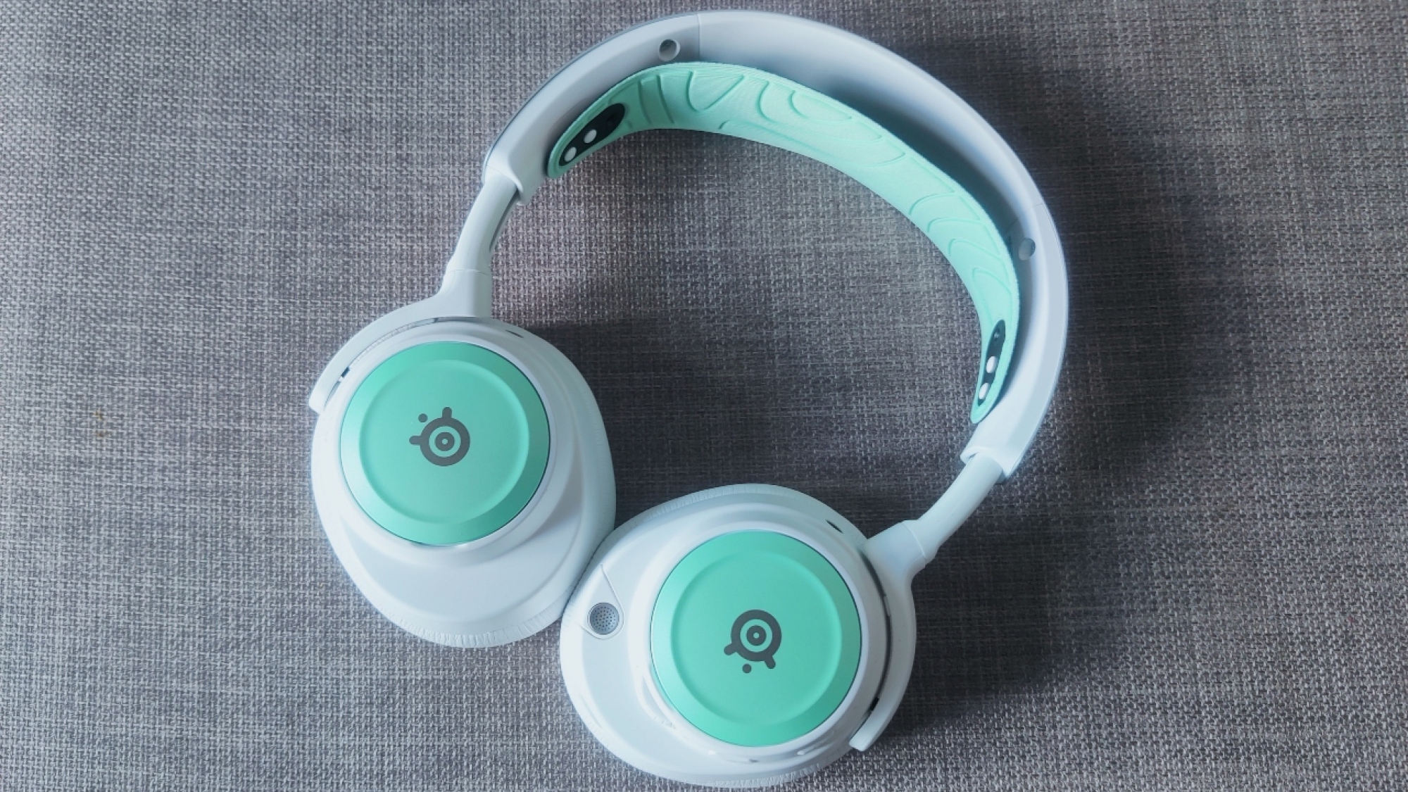 The Steelseries Arctis Nova Pro Wireless In White dengan pelat speaker mint dan ikat kepala, dengan telinga berputar