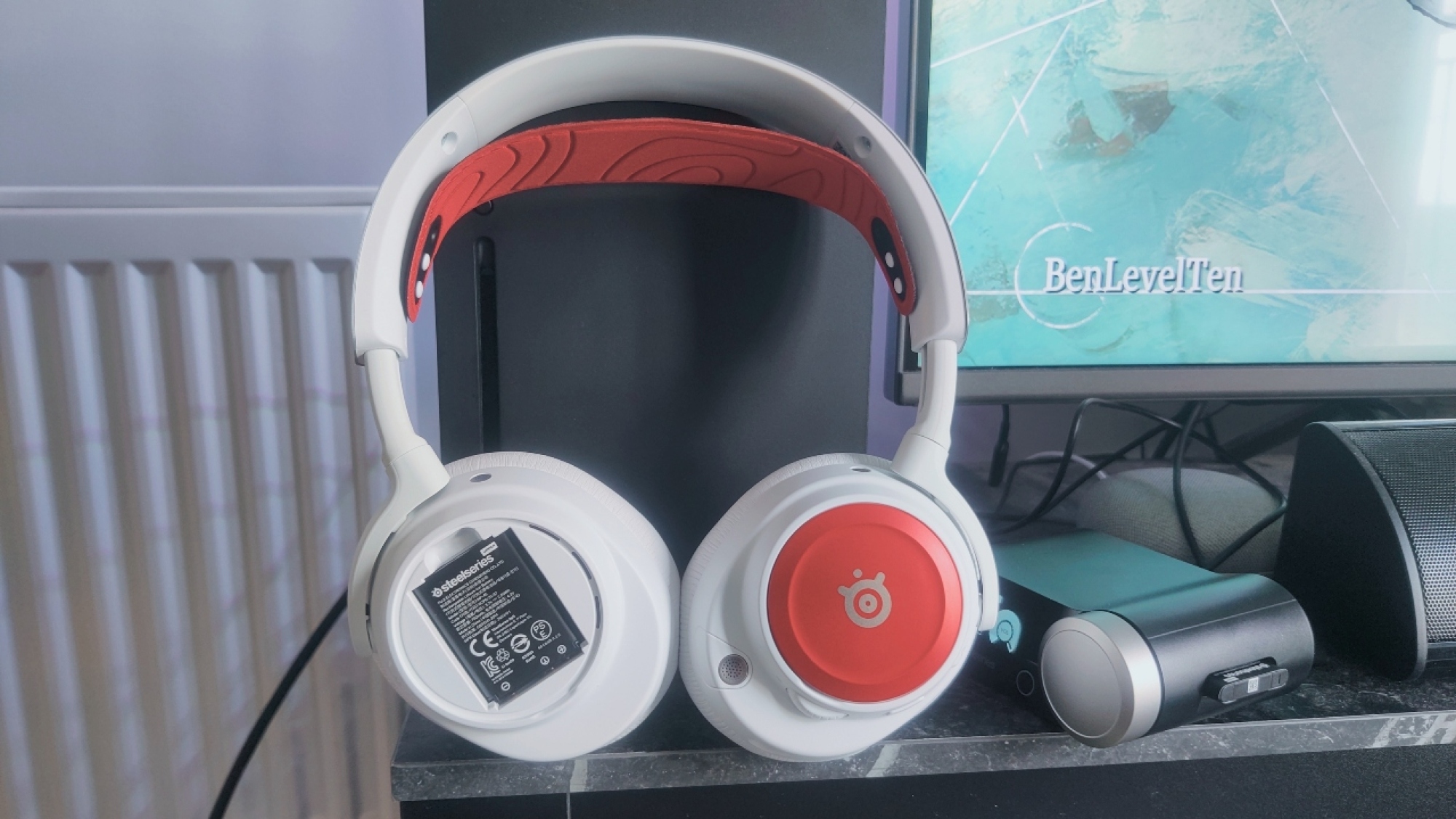 Steelseries Arctis Nova Pro Wireless dengan pelat & ikat kepala speaker merah, dengan satu dilepas menunjukkan baterai yang dapat ditukar